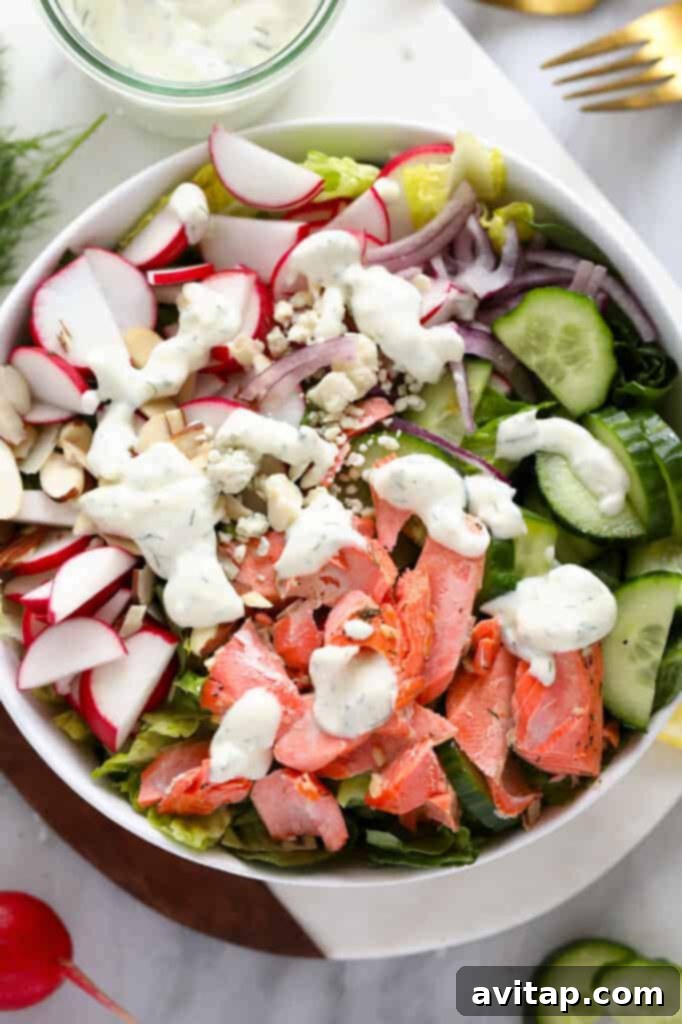 A vibrant salmon salad in a bowl, generously topped with creamy Greek yogurt dressing, with fresh dill and radishes visible, ready to be enjoyed.