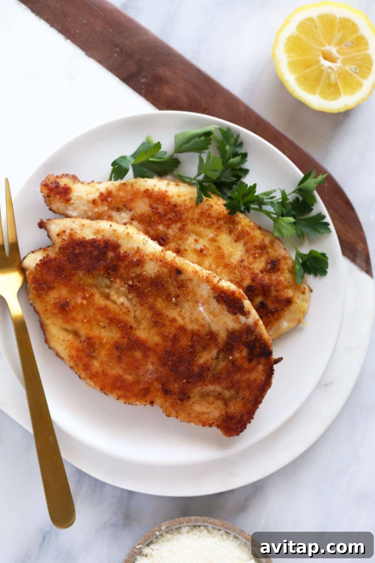 Golden Parmesan Chicken 8 Two cooked and crispy Parmesan crusted chicken breasts served on a white plate, showcasing their inviting texture.