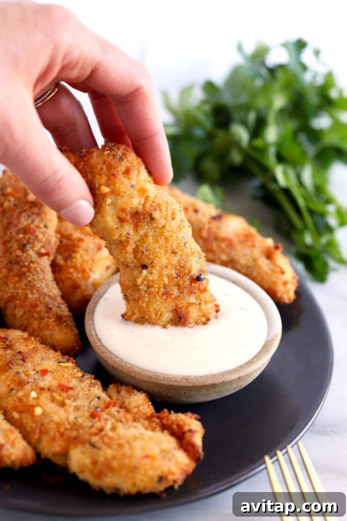 Dipping a golden-brown air fryer chicken tender in a creamy ranch sauce