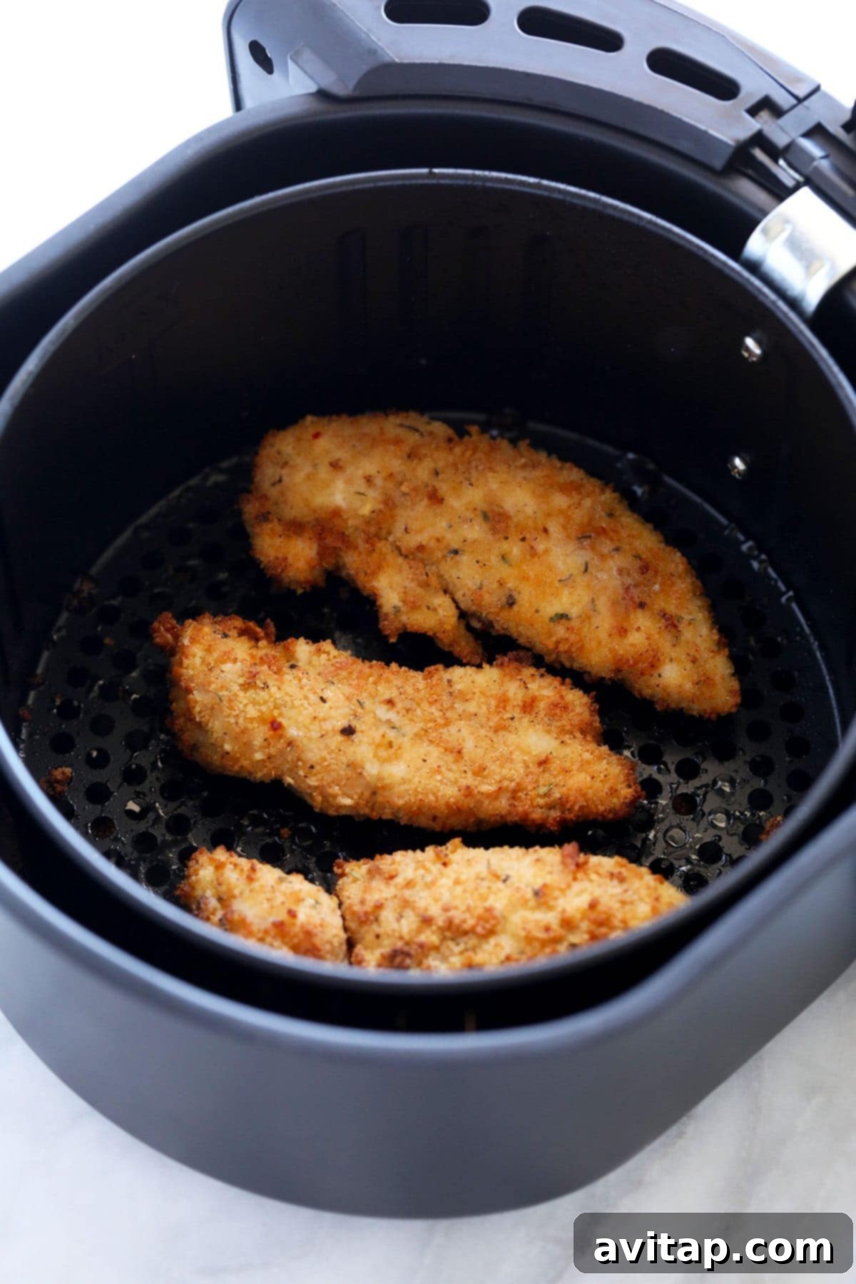 Crispy chicken tenders cooking inside an air fryer basket, achieving a golden hue