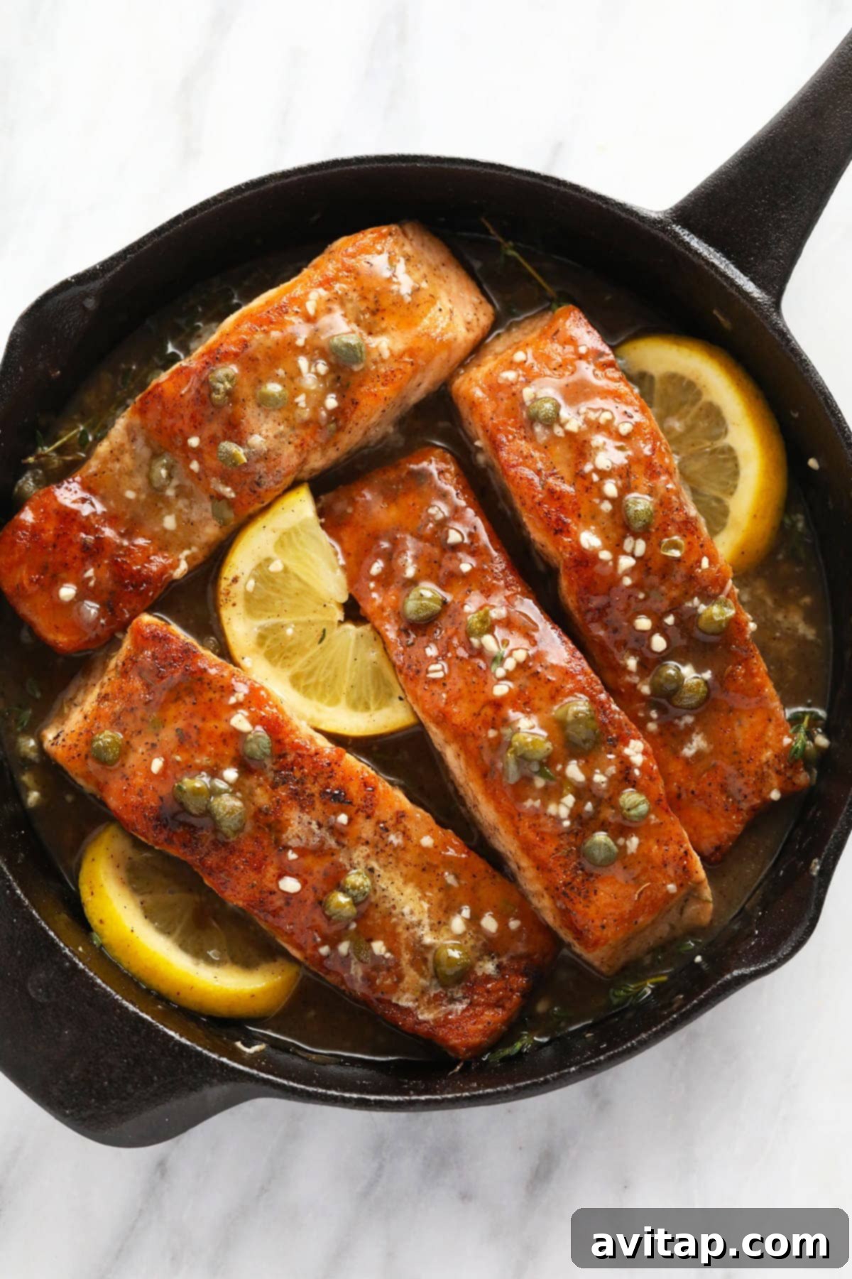 Zesty Lemon Caper Salmon 2 Golden-brown salmon piccata served in a rustic cast iron skillet, garnished with fresh lemon slices and capers.