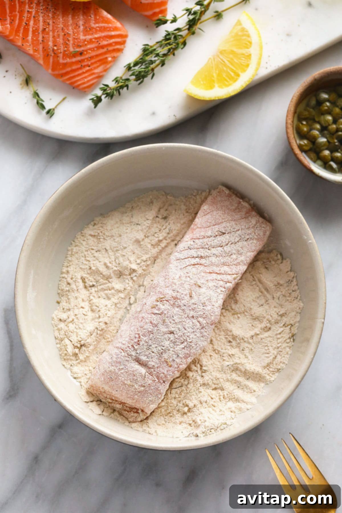 Zesty Lemon Caper Salmon 4 A cook carefully dredging a salmon fillet through a bowl of flour and spices, ensuring an even coating for a crispy sear.