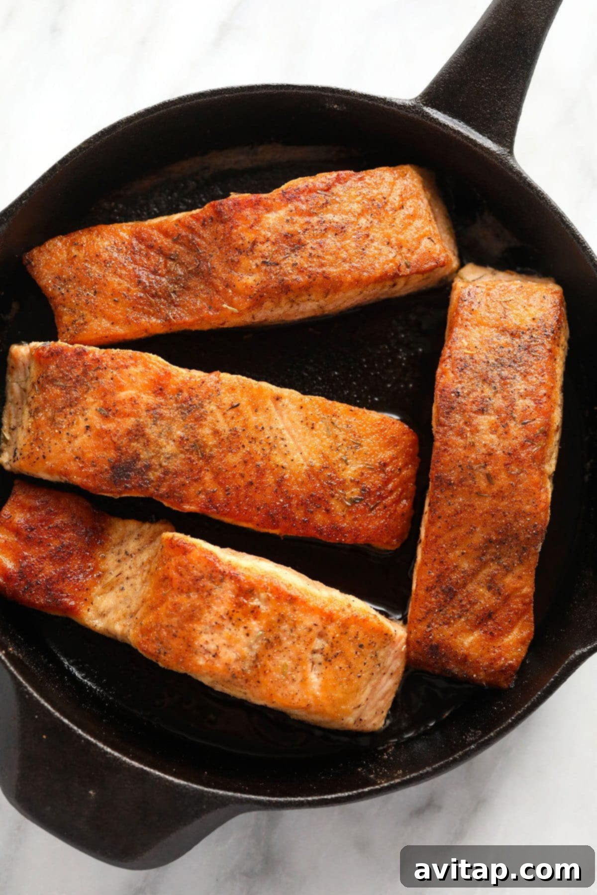 Zesty Lemon Caper Salmon 5 Four golden-seared salmon fillets cooking in a cast iron skillet, ready to be drizzled with piccata sauce.