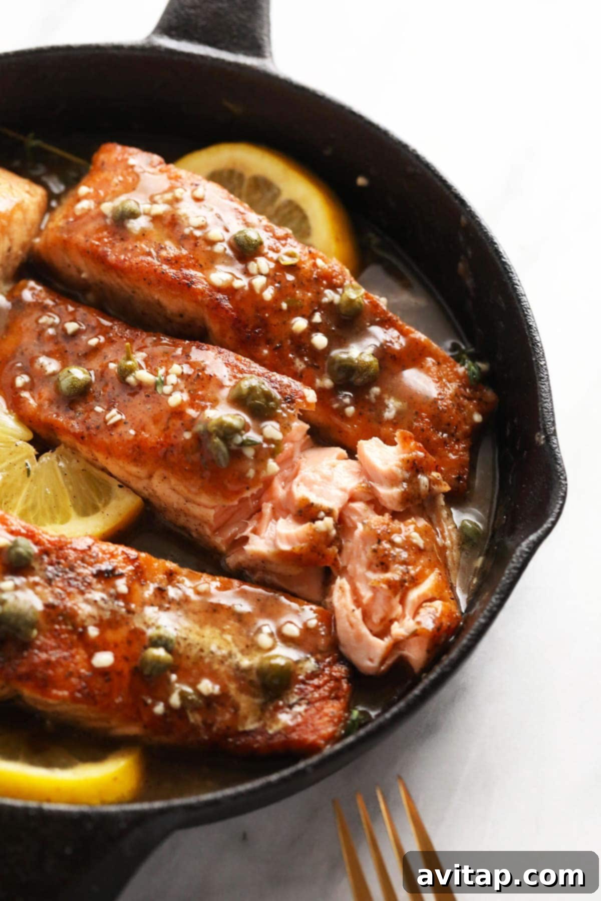 Zesty Lemon Caper Salmon 8 Close-up of perfectly seared salmon piccata in a cast iron pan, showing the flaky fish and rich sauce.
