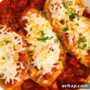 chicken breasts in a white dish with sauce and cheese.