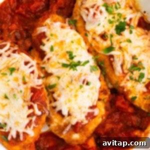 Chicken breasts in a white dish with sauce and cheese.