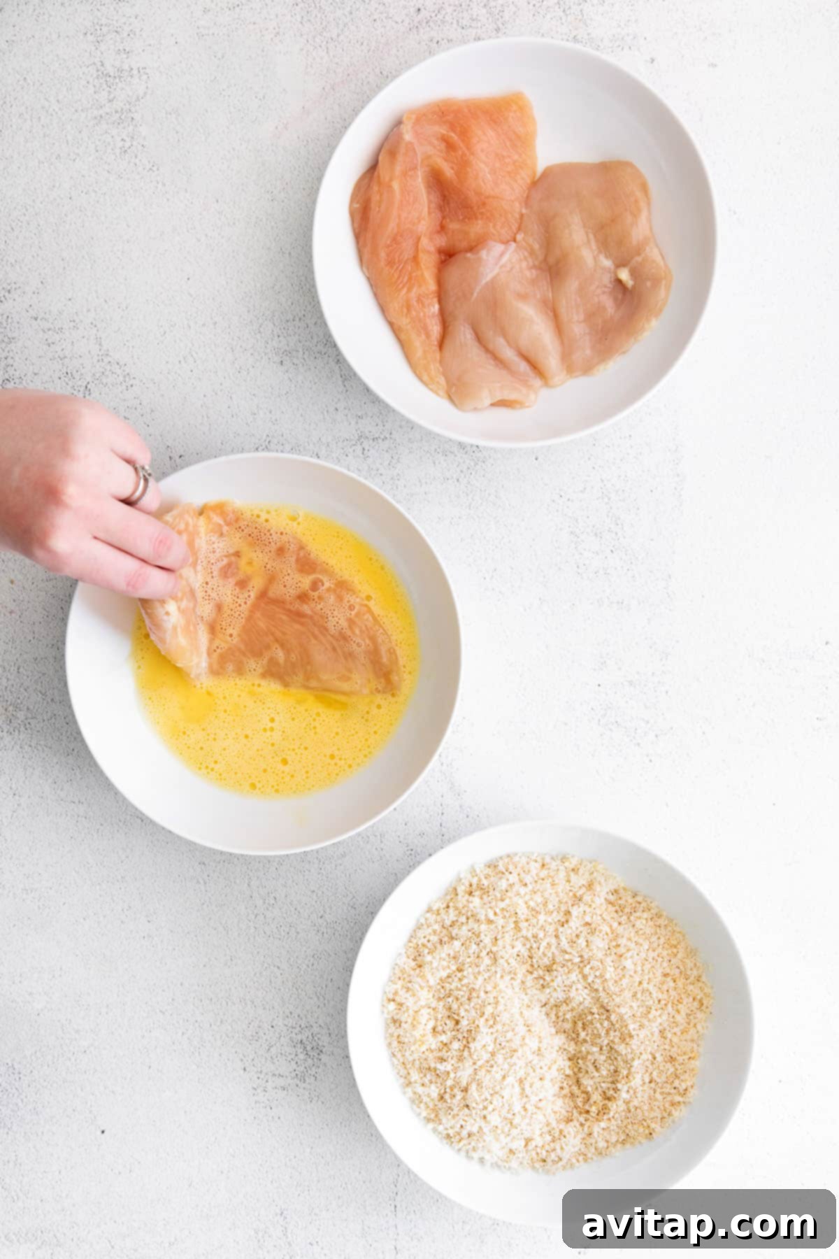 Dipping a chicken breast cutlet into an egg wash.