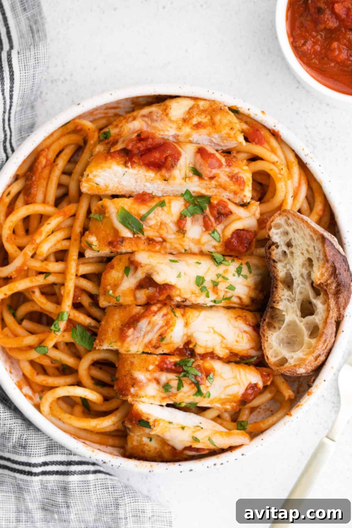 Appetizing image of sliced chicken parmesan on noodles with fresh basil.