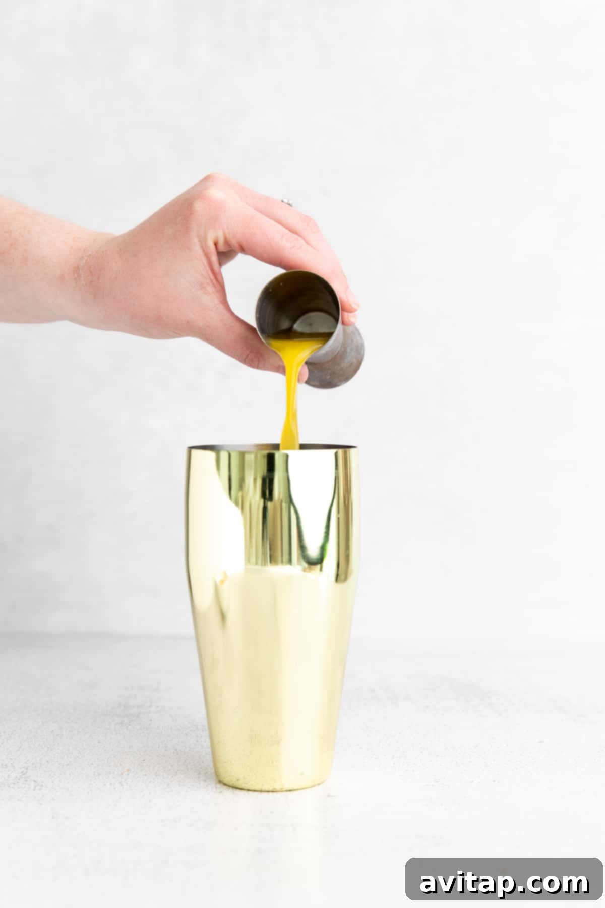 pouring orange juice into a cocktail shaker.