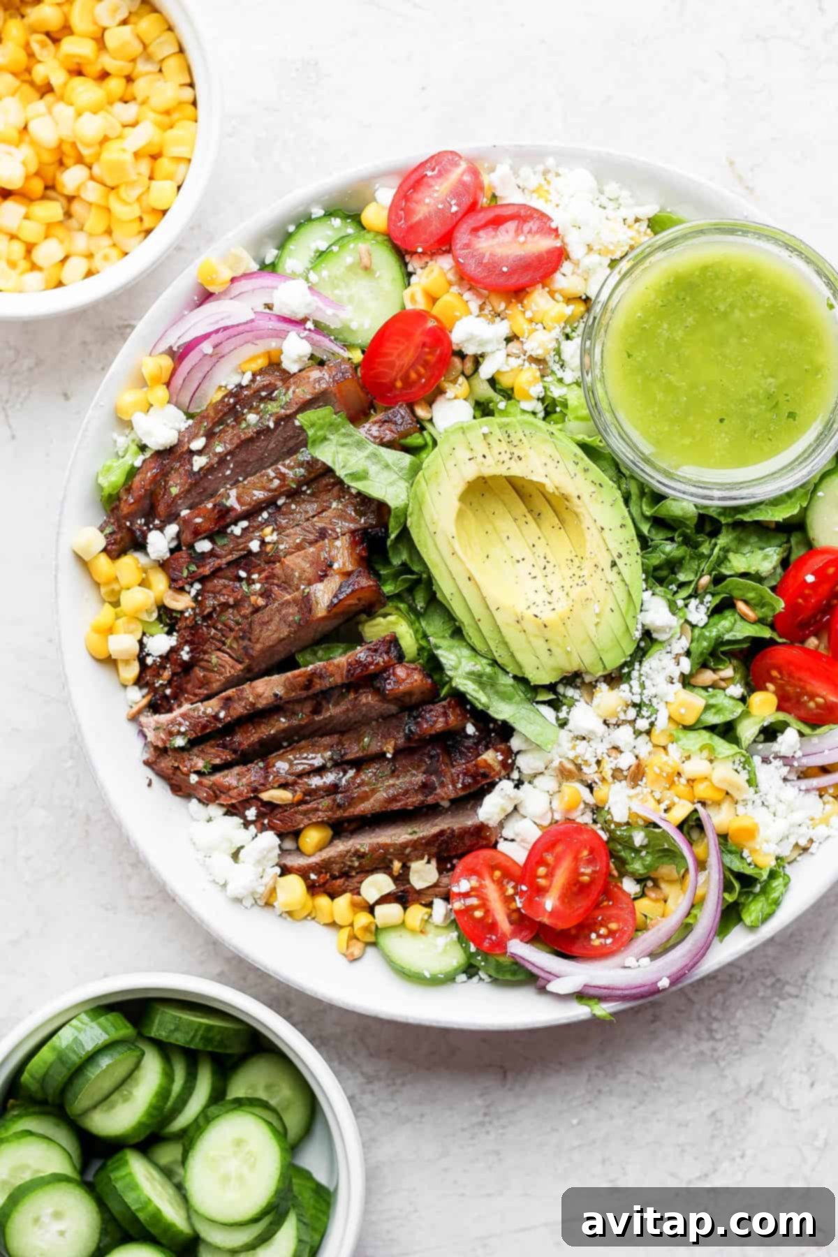 Steak salad in a bowl with dressing, featuring grilled steak, corn, avocado, and goat cheese.