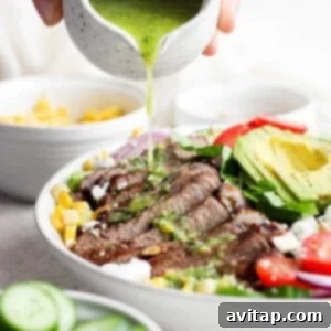 Pouring green dressing over a colorful salad in a large bowl.