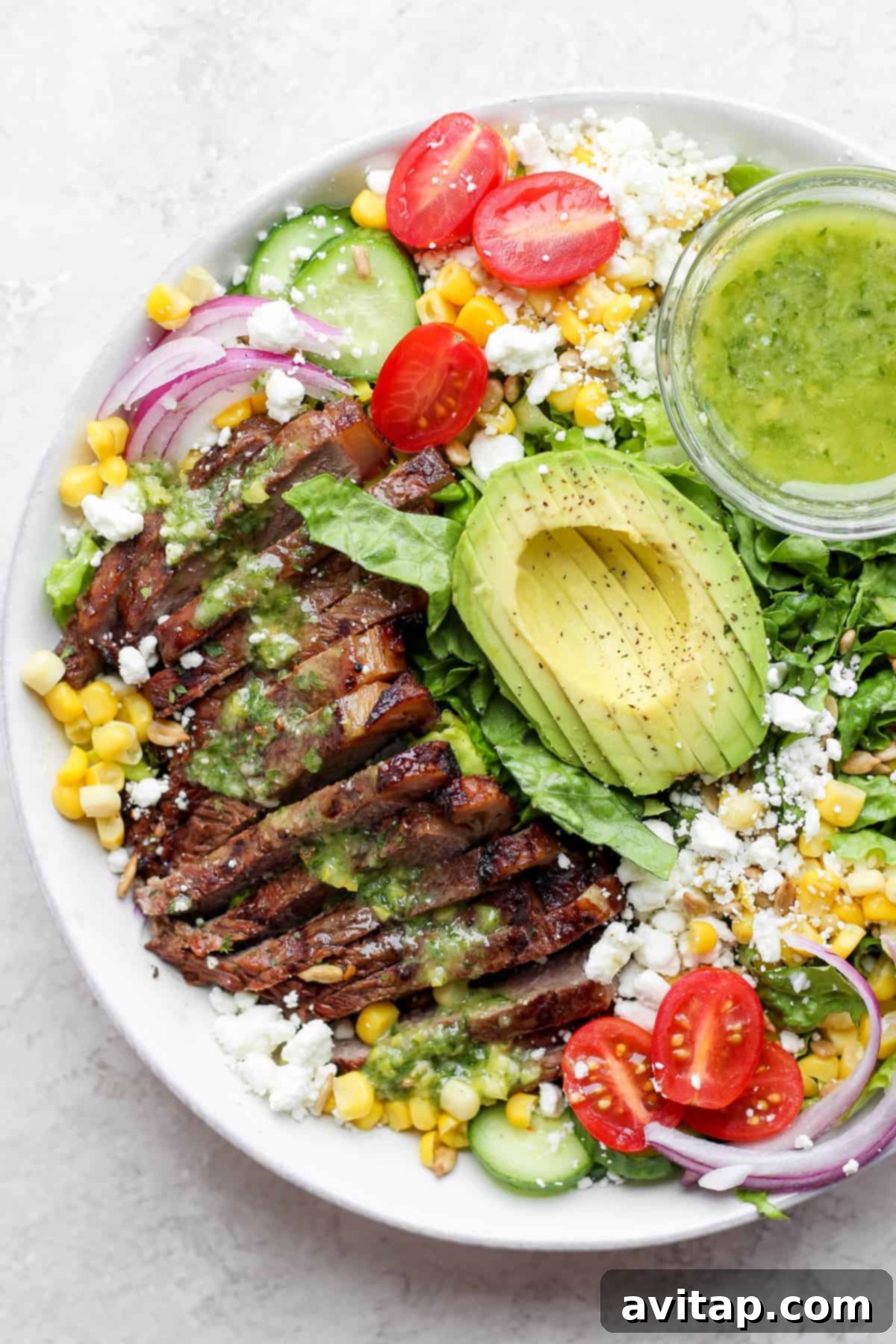 A large bowl of steak salad, garnished with sliced steak, corn, avocado, and goat cheese.