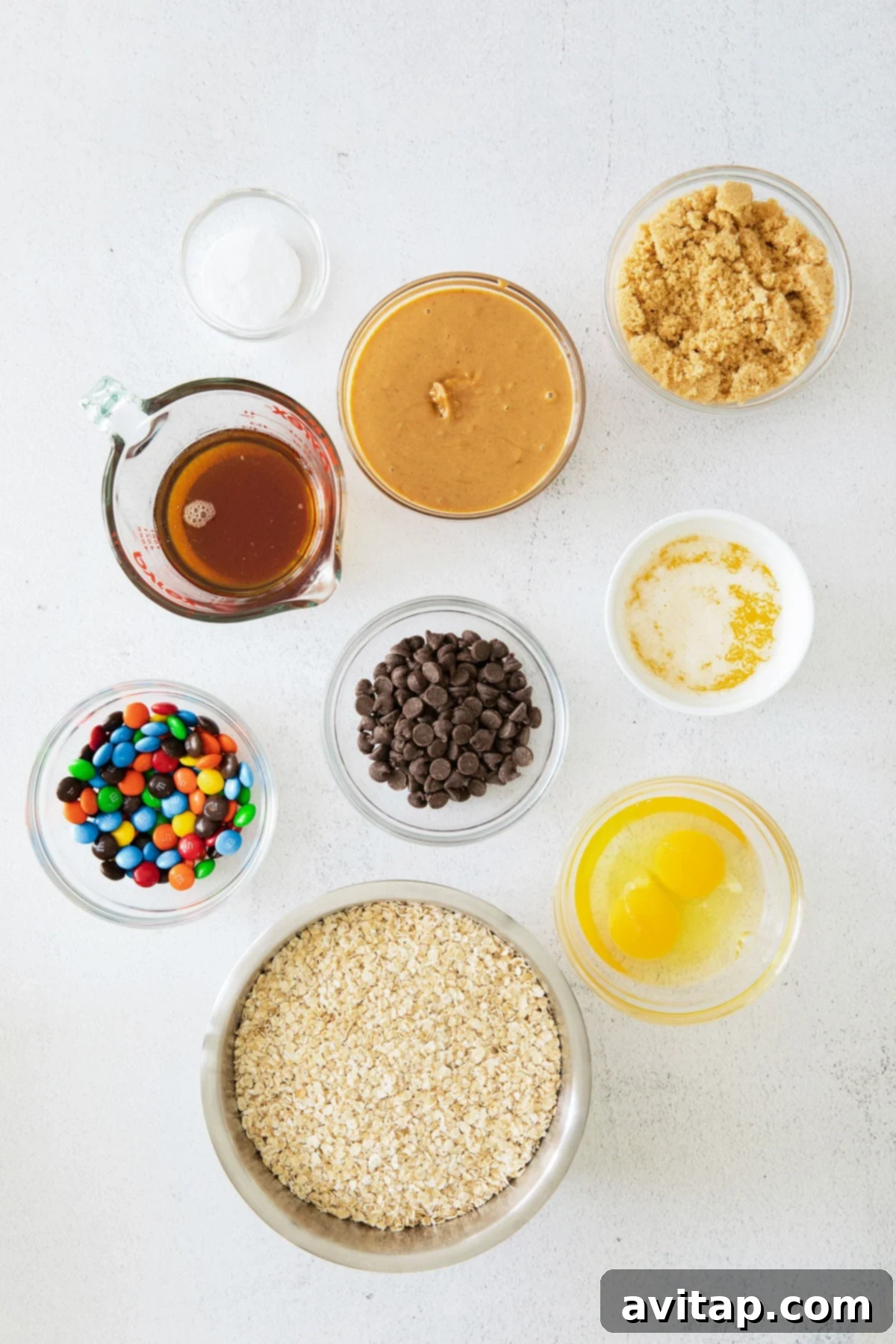 A visual guide to the wholesome and delicious ingredients required for baking flourless Monster Cookies. Close-up of essential monster cookie ingredients laid out, including a bowl of oats, a jar of peanut butter, chocolate chips, and colorful M&M's.