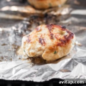 Chicken burger patties on a grill grate with tin foil, sizzling.