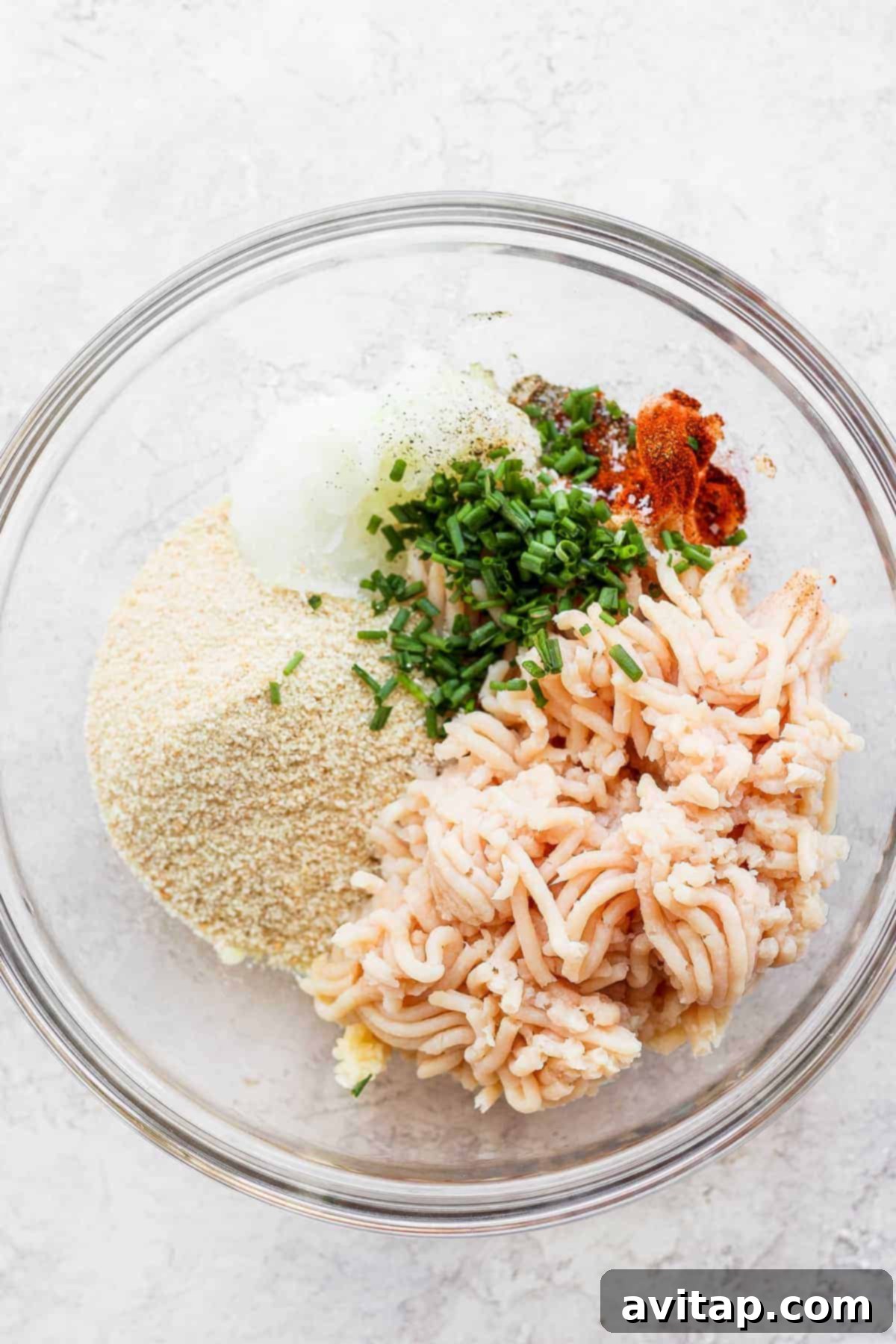 Bowl filled with ground chicken, breadcrumbs, finely chopped onion, and fresh chives, ready for mixing.