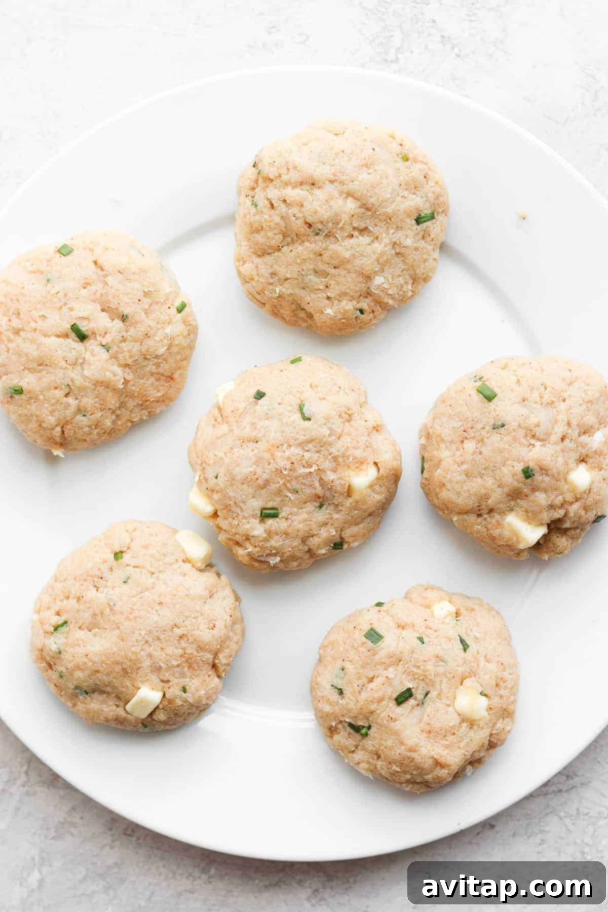 Six perfectly formed ground chicken burger patties arranged on a plate, ready for grilling.