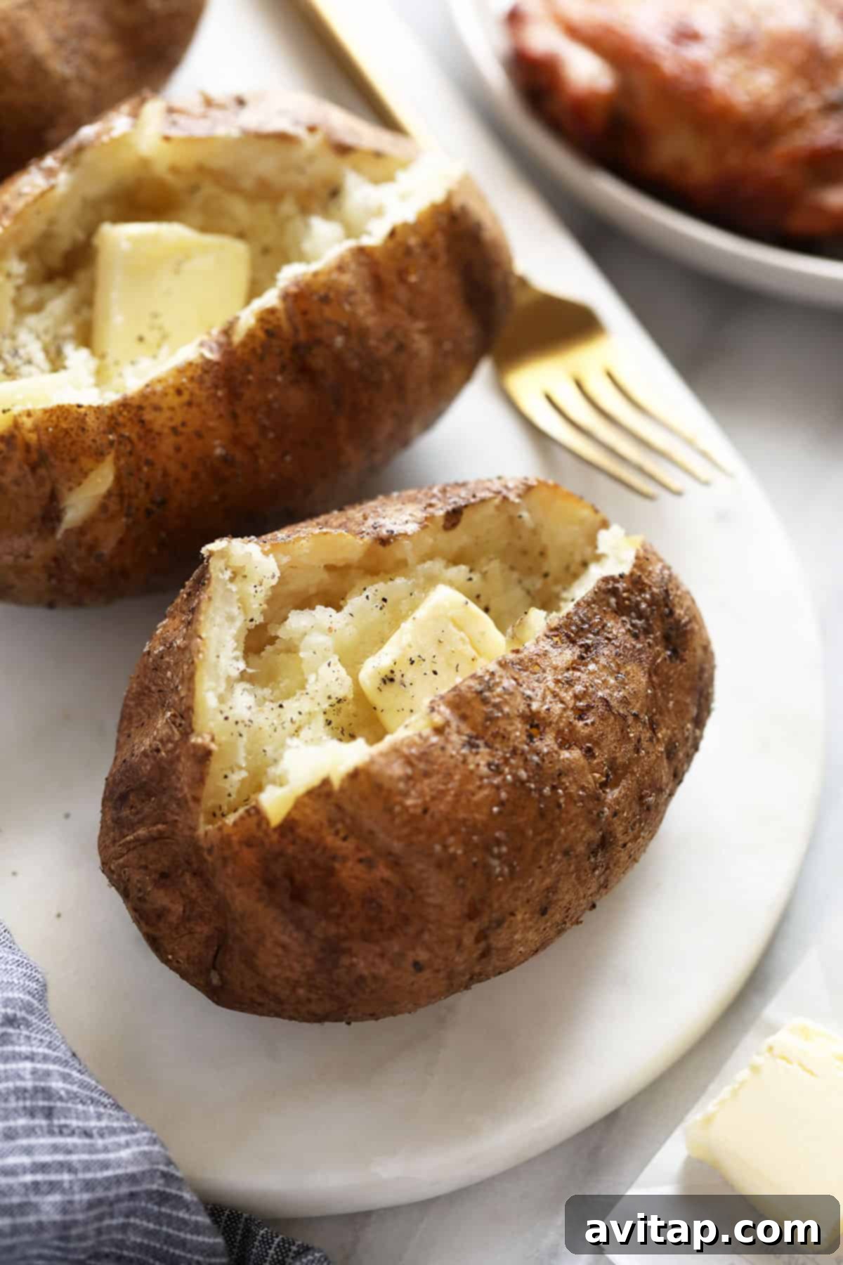 A perfectly smoked baked potato, split open, showing melted butter, a sprinkle of salt, and freshly ground pepper inside.