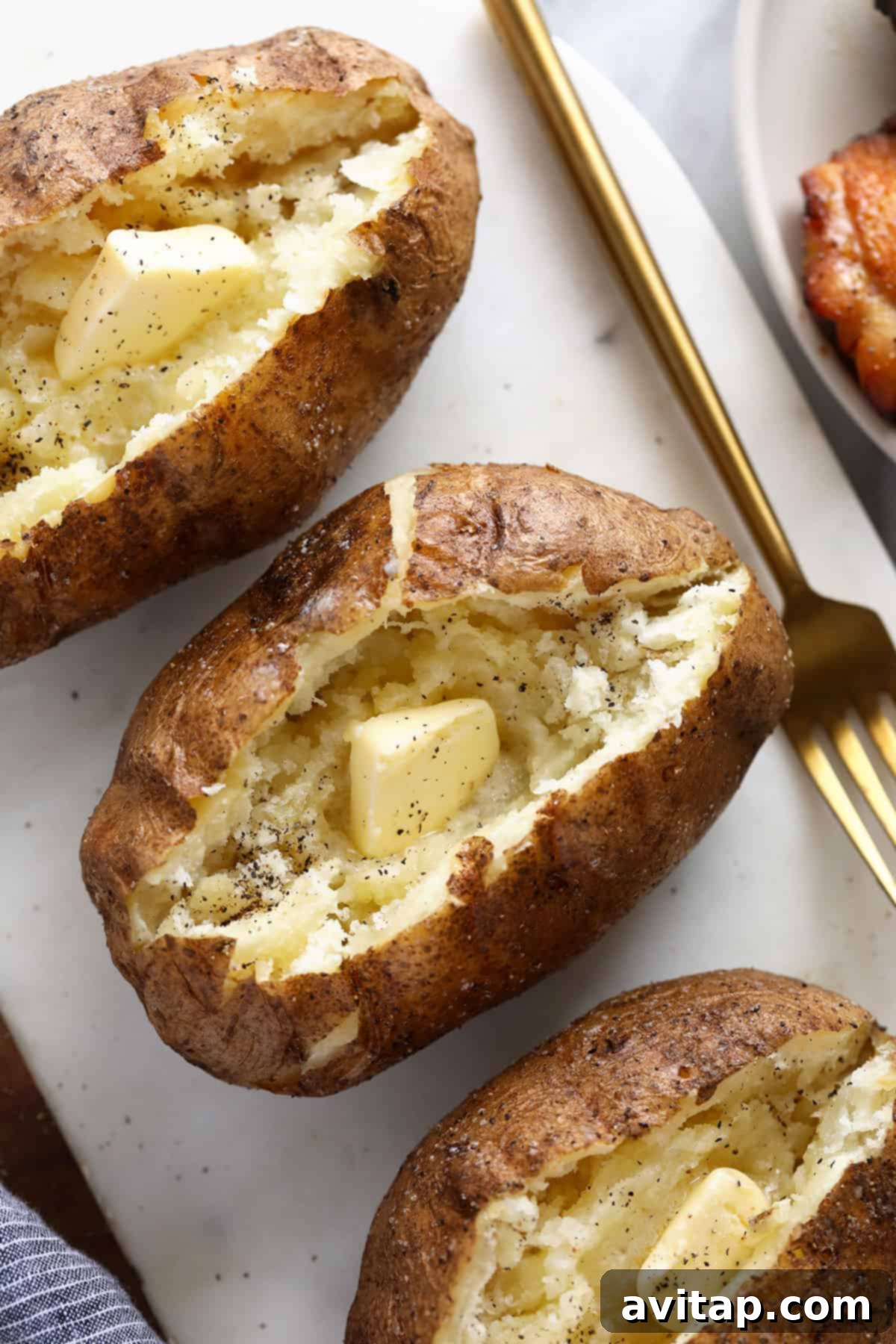Three perfectly smoked baked potatoes resting on a wooden cutting board with a side of creamy butter, ready to be sliced and customized with toppings.