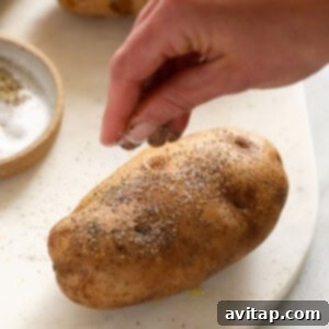 A person is sprinkling salt and pepper on some oil-coated raw potatoes on a tray, preparing them for smoking.