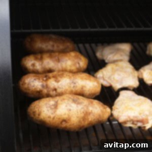 A BBQ grill with golden-brown chicken thighs and perfectly smoked baked potatoes cooking on the grates.