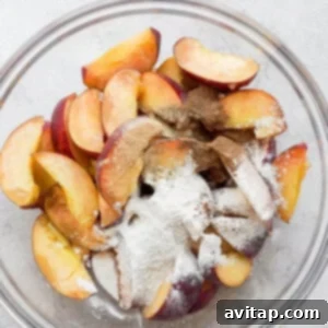The Ultimate Peach Crisp 2 Close-up of sliced peaches coated with flour and spices in a large mixing bowl, showing the even distribution of ingredients before baking.