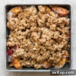The Ultimate Peach Crisp 4 Unbaked peach crisp in a glass baking dish, showing the peach filling completely covered with the raw, golden crumble topping, ready to enter the oven.