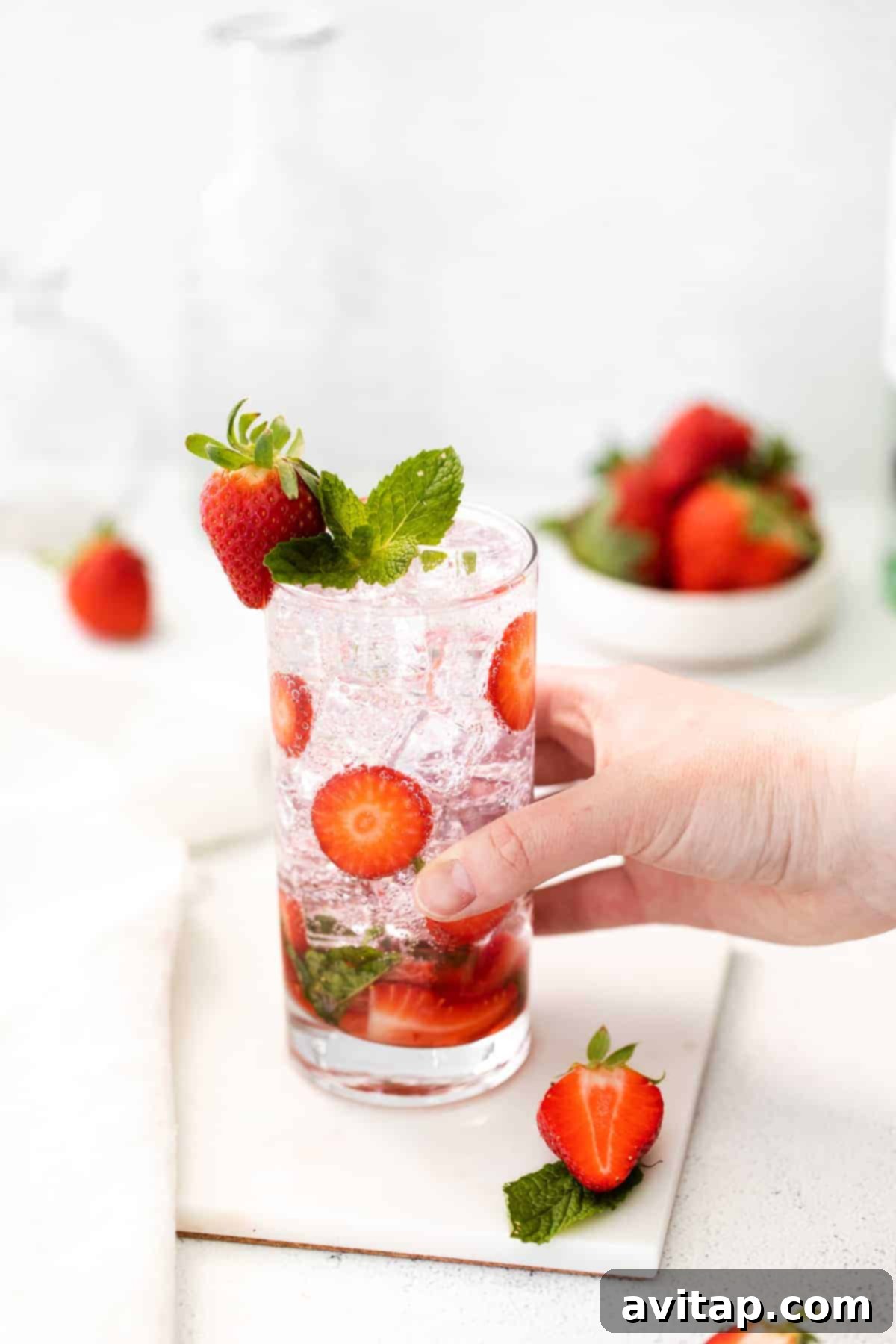 Hand holding a strawberry mojito glass, showcasing its vibrant color and garnish