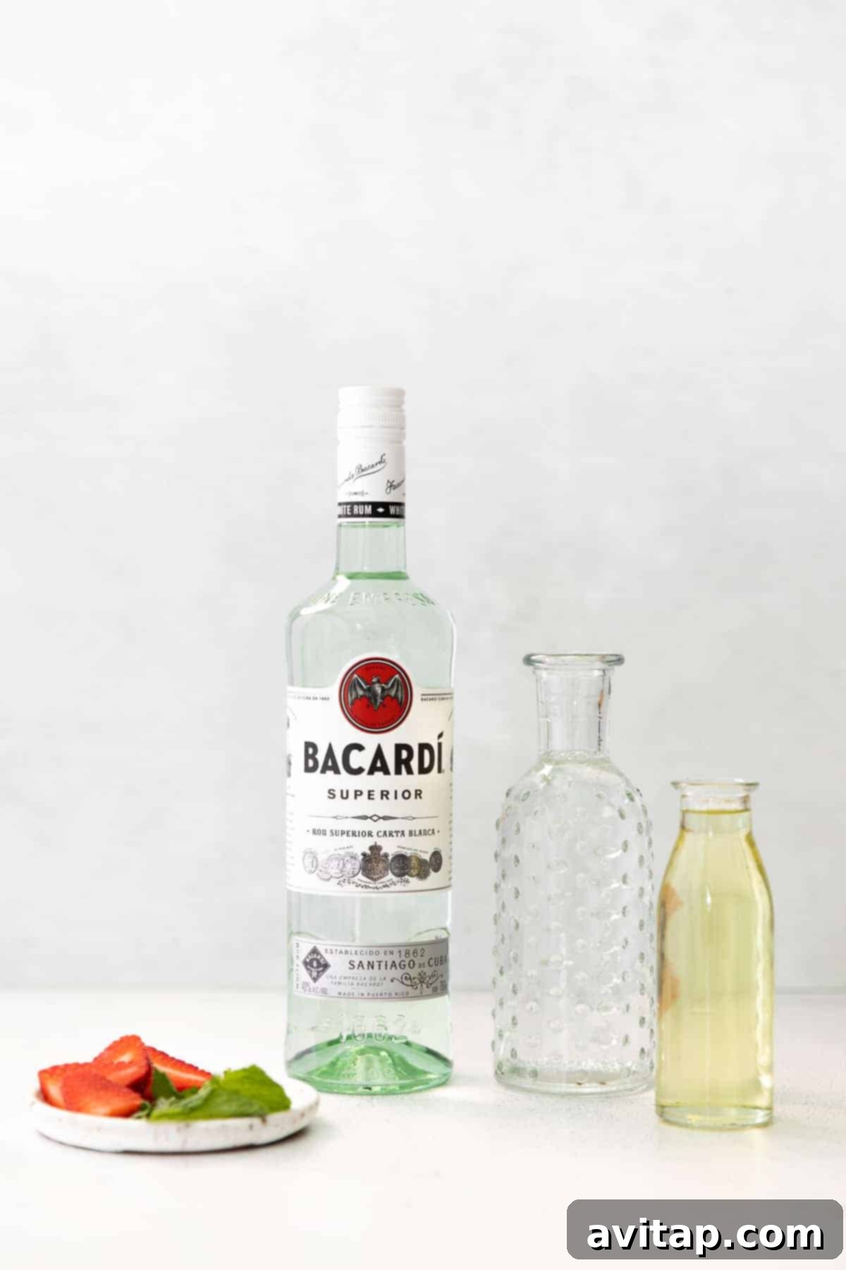 Fresh cocktail ingredients, including strawberries, mint, rum, and simple syrup, laid out on a countertop