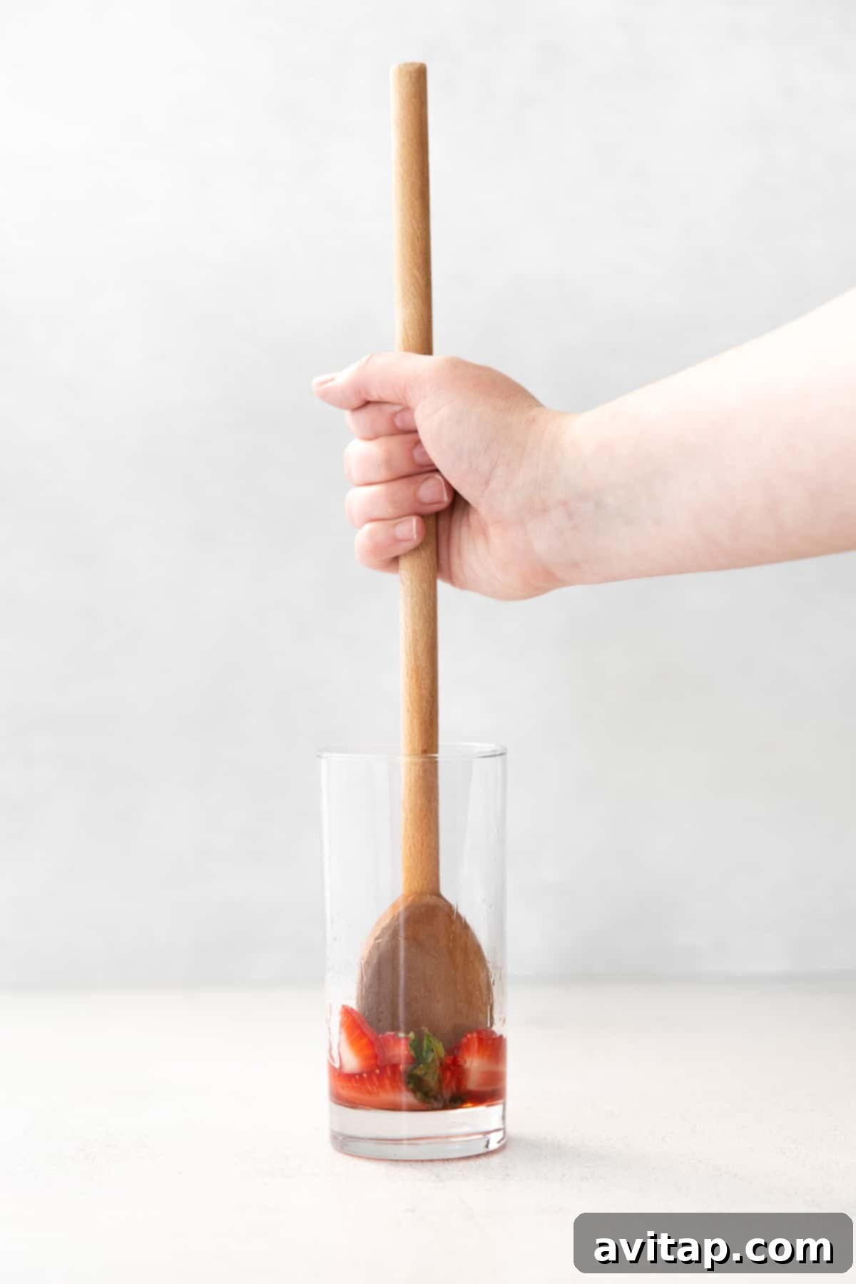 Hand muddling fresh strawberries and mint in a cocktail glass