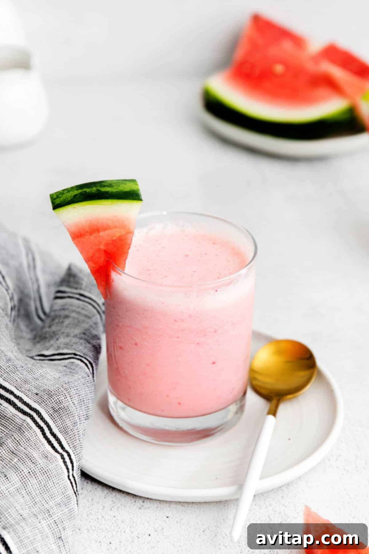 A vibrant red watermelon smoothie in a clear glass, garnished with a fresh slice of watermelon on the rim.