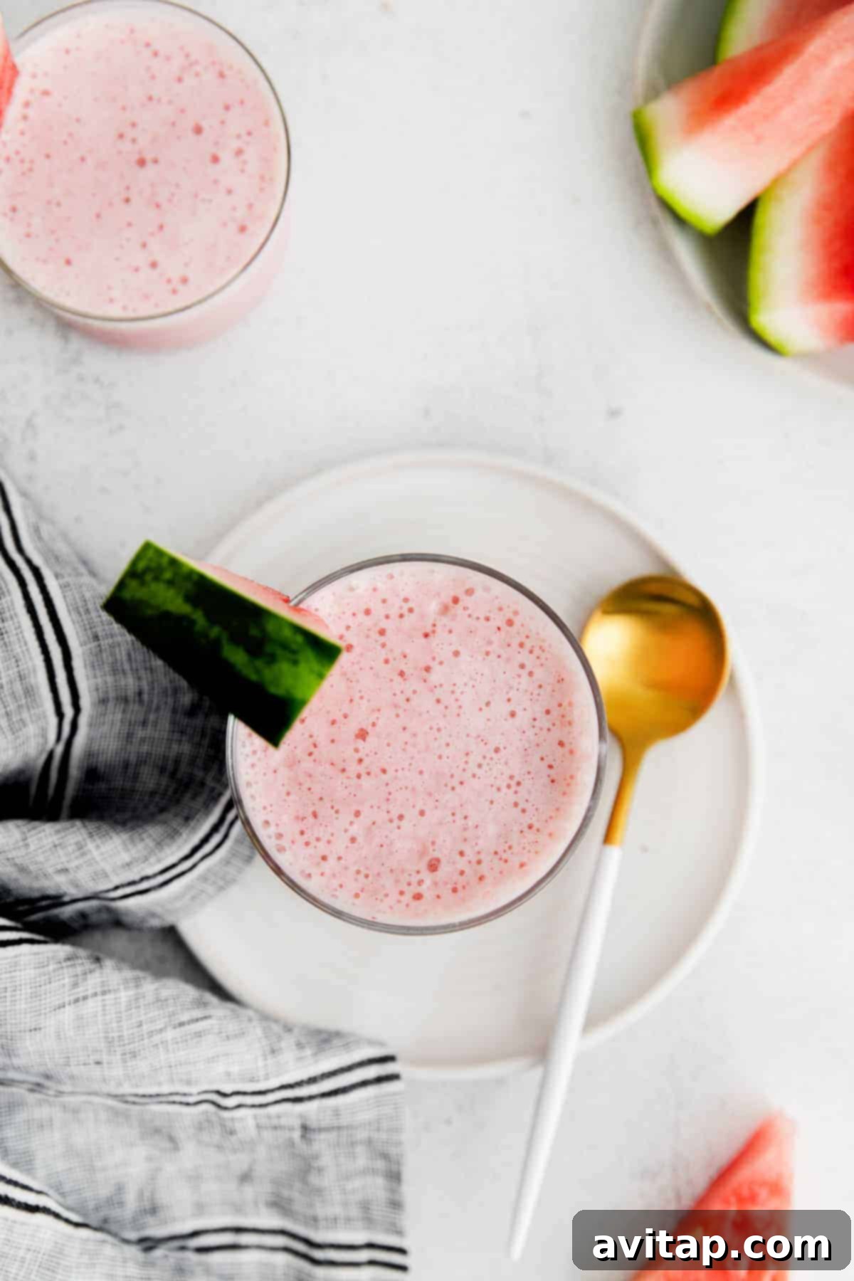 A single glass of vibrant watermelon smoothie sitting on a light wooden surface, with soft natural light.