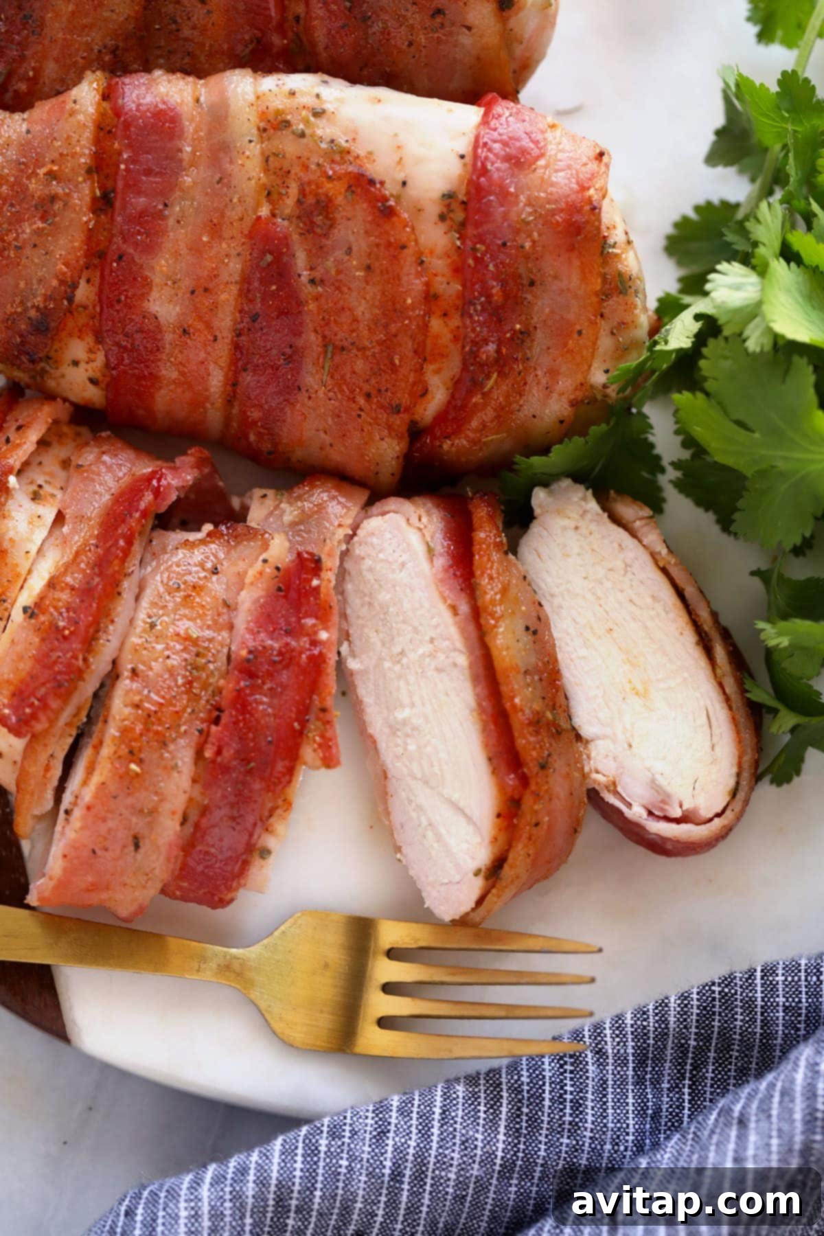 Sliced chicken wrapped chicken breast on plate A sliced, perfectly cooked bacon wrapped chicken breast served on a plate, revealing the juicy interior, garnished with fresh herbs.