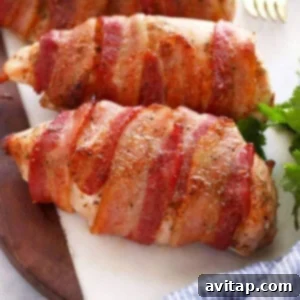 Golden Crispy Bacon Wrapped Chicken 2 Bacon wrapped chicken breasts on a cutting board.