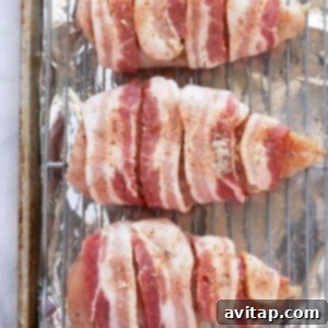 Golden Crispy Bacon Wrapped Chicken 4 Bacon wrapped chicken breasts on a baking sheet.