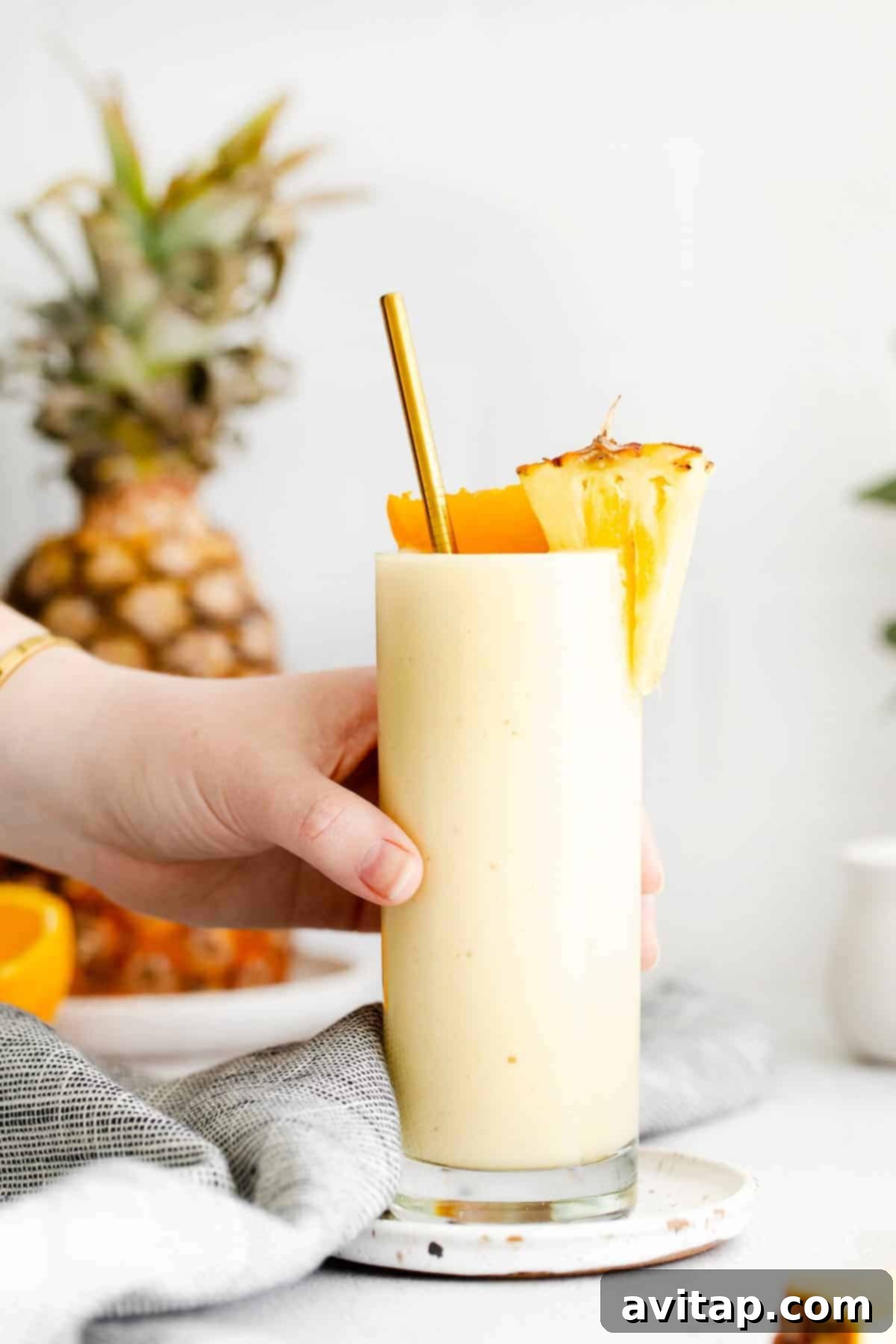 A hand holding a glass of refreshing pineapple smoothie, ready to be enjoyed on a warm day.