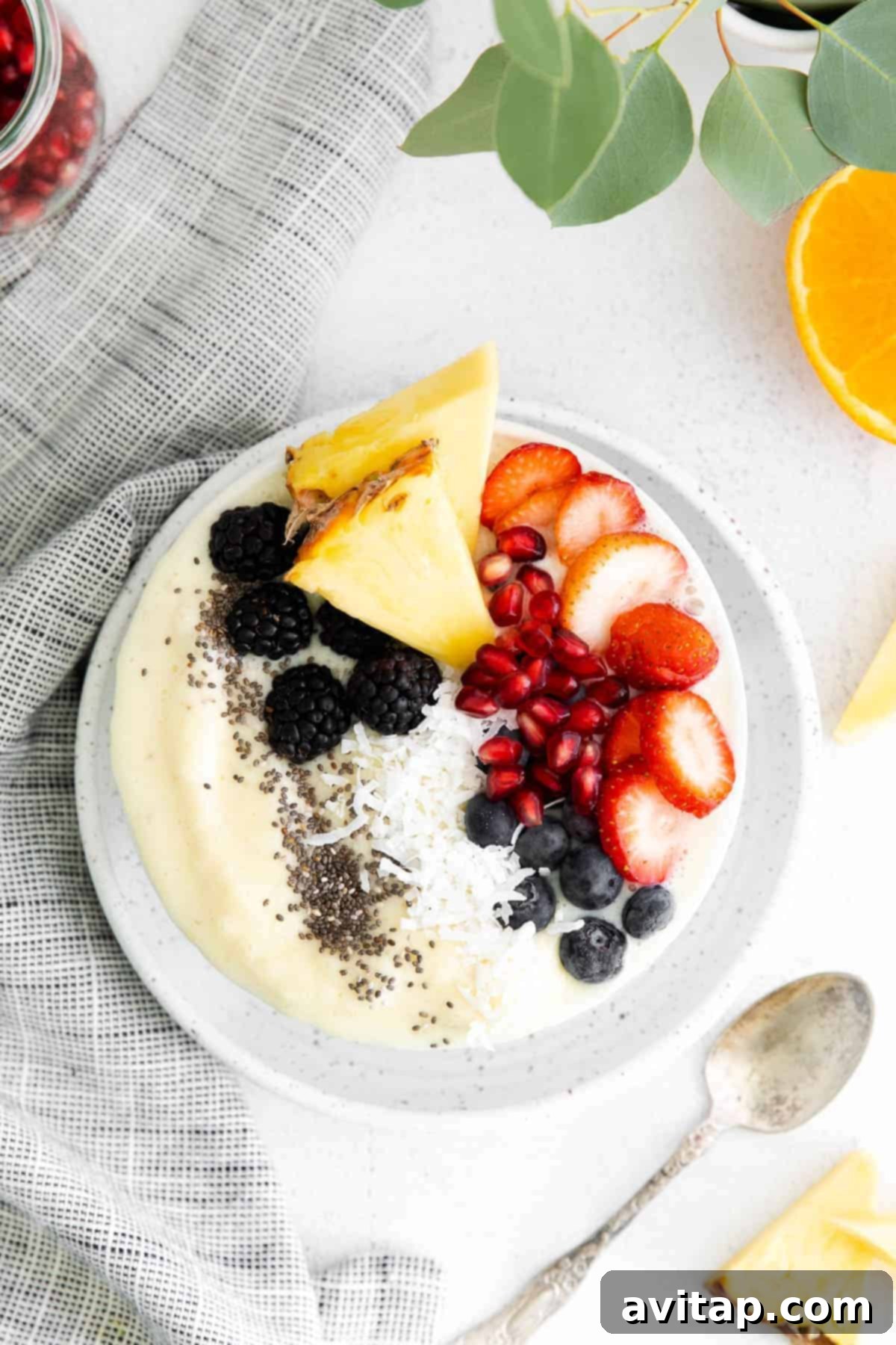 A beautifully arranged pineapple smoothie bowl topped with a variety of fresh berries and seeds.
