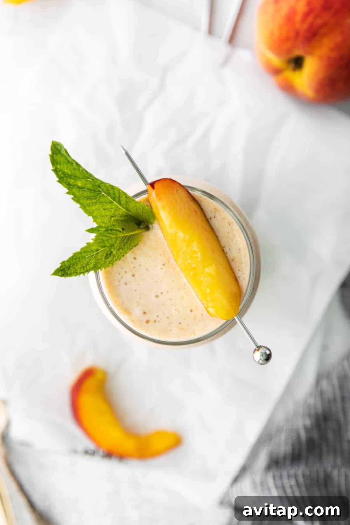 This peach smoothie tastes just like dessert, but it's healthy and made with just 5 ingredients. Make this smoothie all summer long with frozen peaches, banana, cinnamon, almond milk, and vanilla. A vibrant peach smoothie, topped with a fresh peach slice, held against a bright, clean background