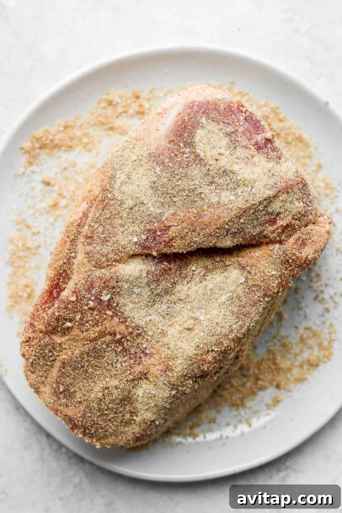 Seasoning Your Pork Shoulder for Ultimate Flavor A boneless pork shoulder roast generously coated with a savory and sweet dry rub on a white plate, ready for searing.