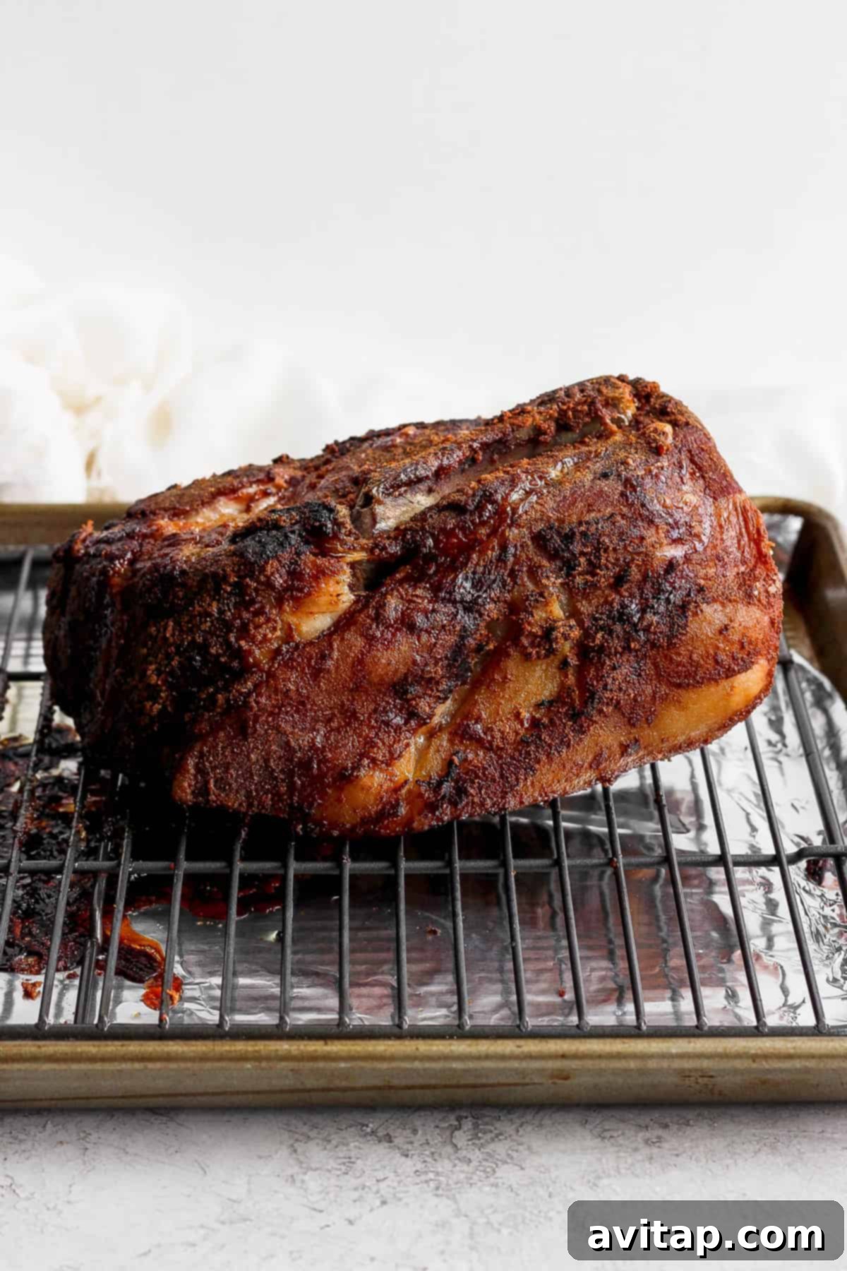 Slow cooked pork shoulder resting on a wire rack over a baking sheet, showing its crispy exterior.