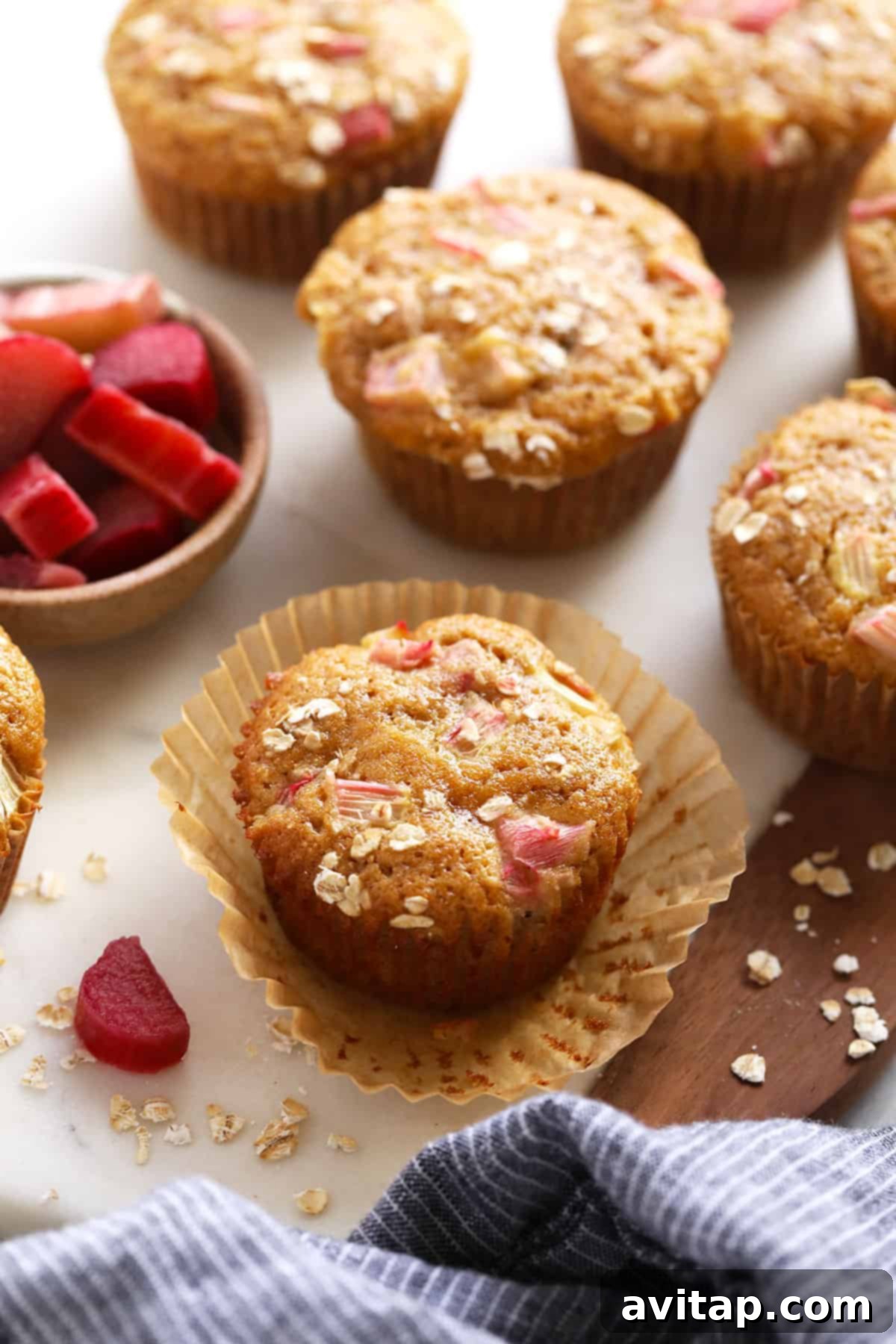 Freshly baked rhubarb muffins cooling on a wire rack, with some scattered rhubarb stalks and fresh berries in the background. The muffins are golden brown and perfectly risen.