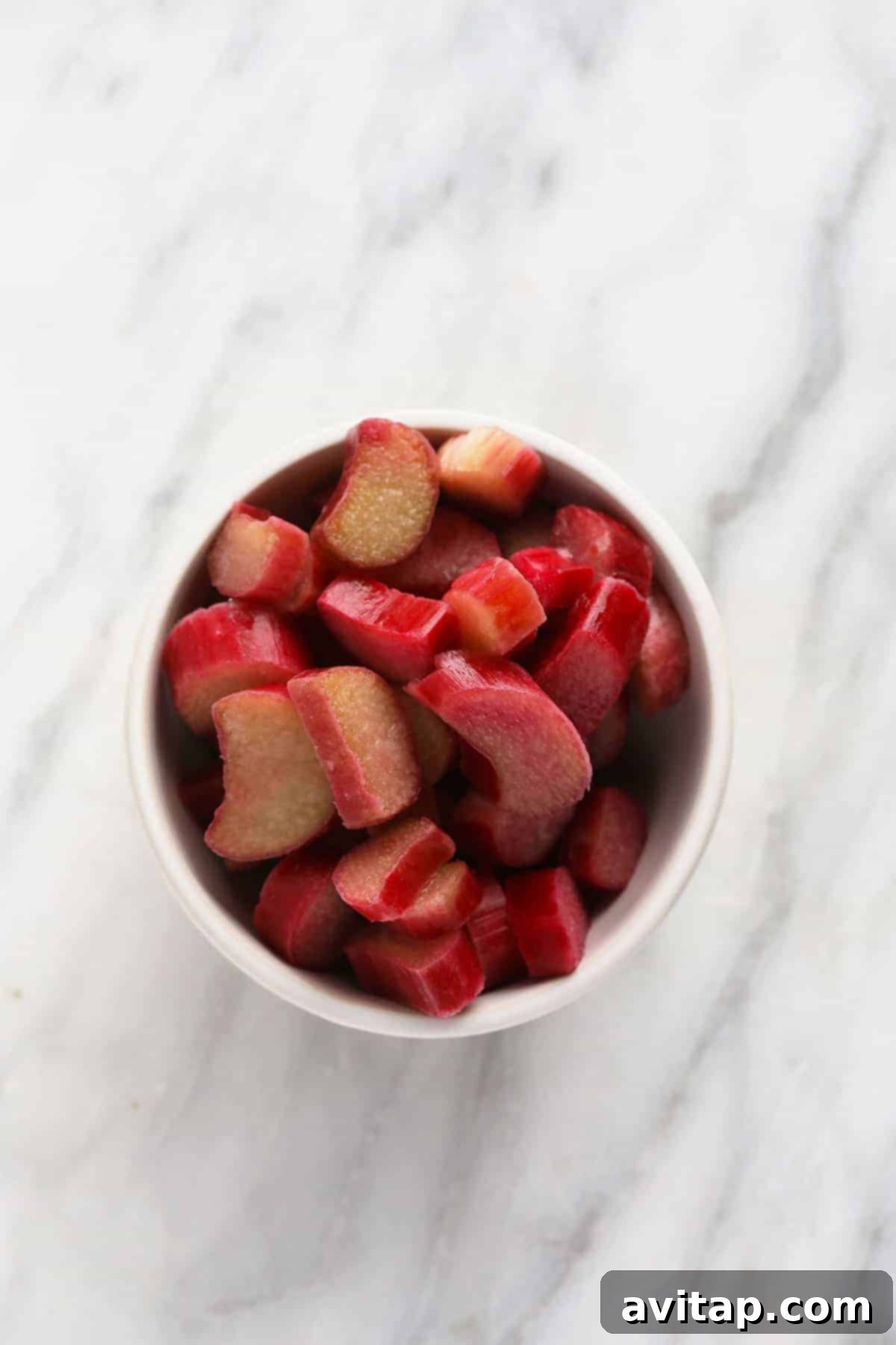 A ceramic bowl generously filled with vibrant, freshly diced rhubarb chunks, ready to be incorporated into a delicious muffin batter.