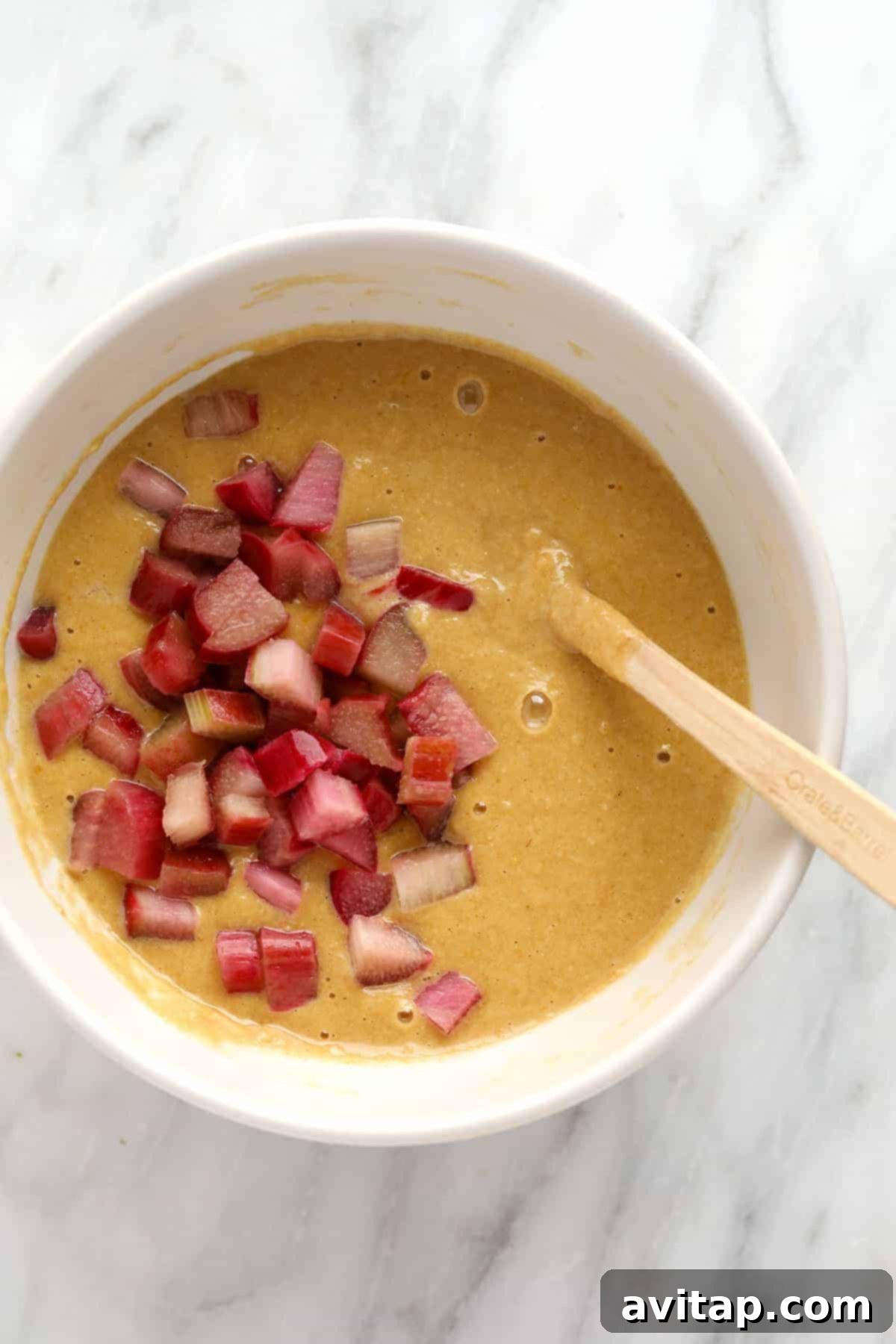 Close-up view of fluffy rhubarb muffin batter in a large mixing bowl, showcasing the diced rhubarb pieces.
