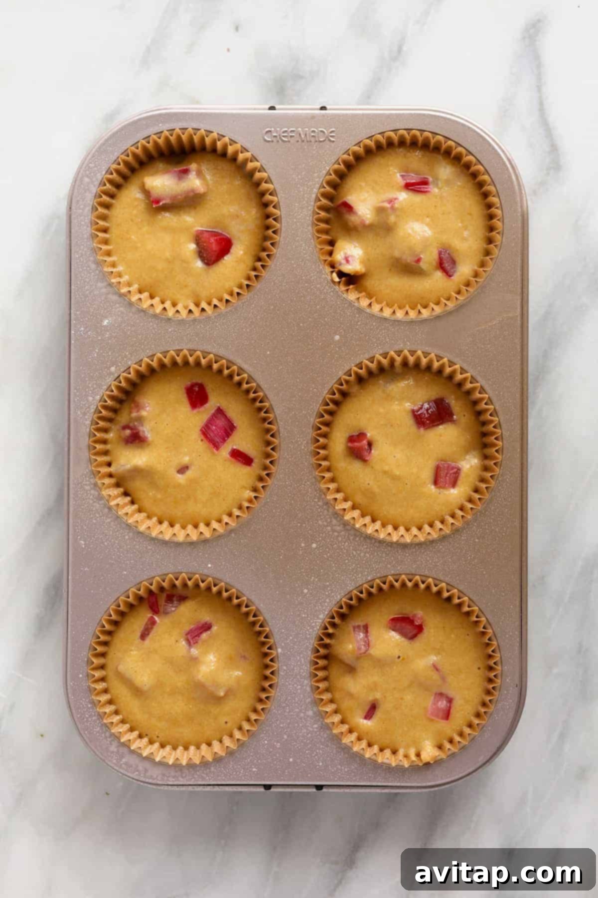 Rhubarb muffin batter meticulously portioned into a muffin pan, filling each cup and ready for the oven.