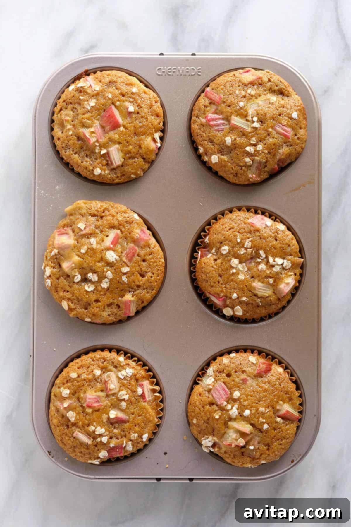 A muffin tin filled with freshly baked, golden-brown rhubarb muffins, showing their perfect rise and inviting texture.
