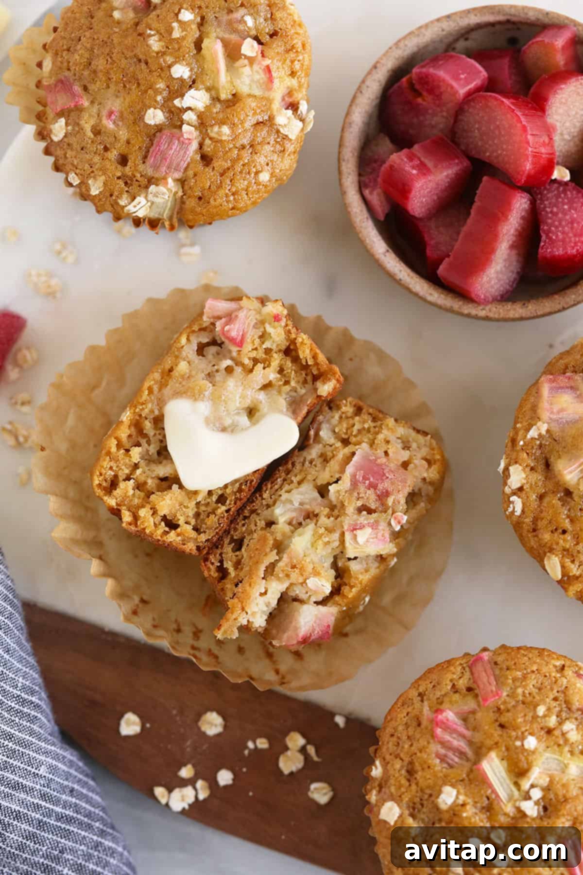 A single rhubarb muffin on a white plate, topped with a melting pat of butter, offering a comforting and delicious experience.