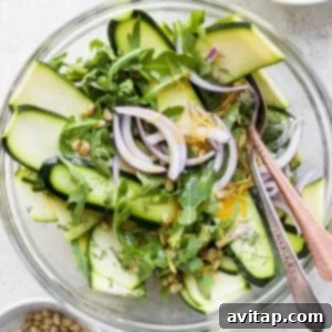 A beautifully presented zucchini salad in a white bowl, garnished with fresh herbs and pine nuts, captured from an appealing angle.