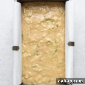 A metal loaf pan filled with zucchini bread batter, placed on a baking sheet, ready to go into the oven.