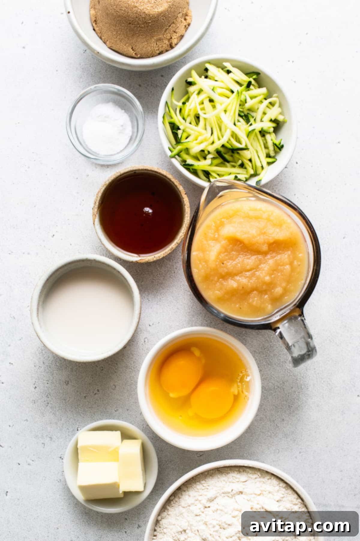 A rustic wooden table displaying various bowls, some containing ingredients for baking, and a loaf of fresh zucchini bread cooling on a rack, highlighting the preparation process.