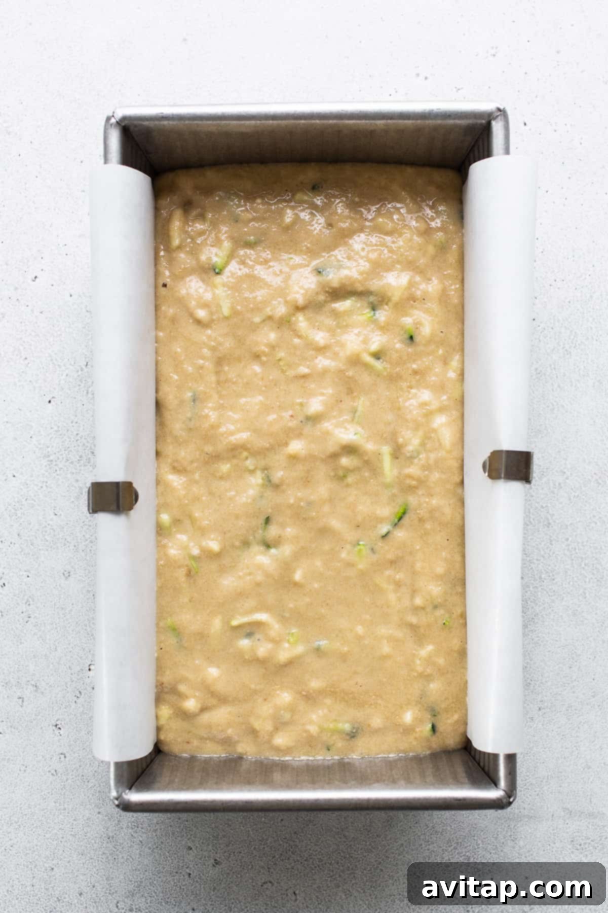 A freshly baked, golden-brown zucchini bread loaf, still in its metal pan, cooling on a wire rack on a kitchen table.