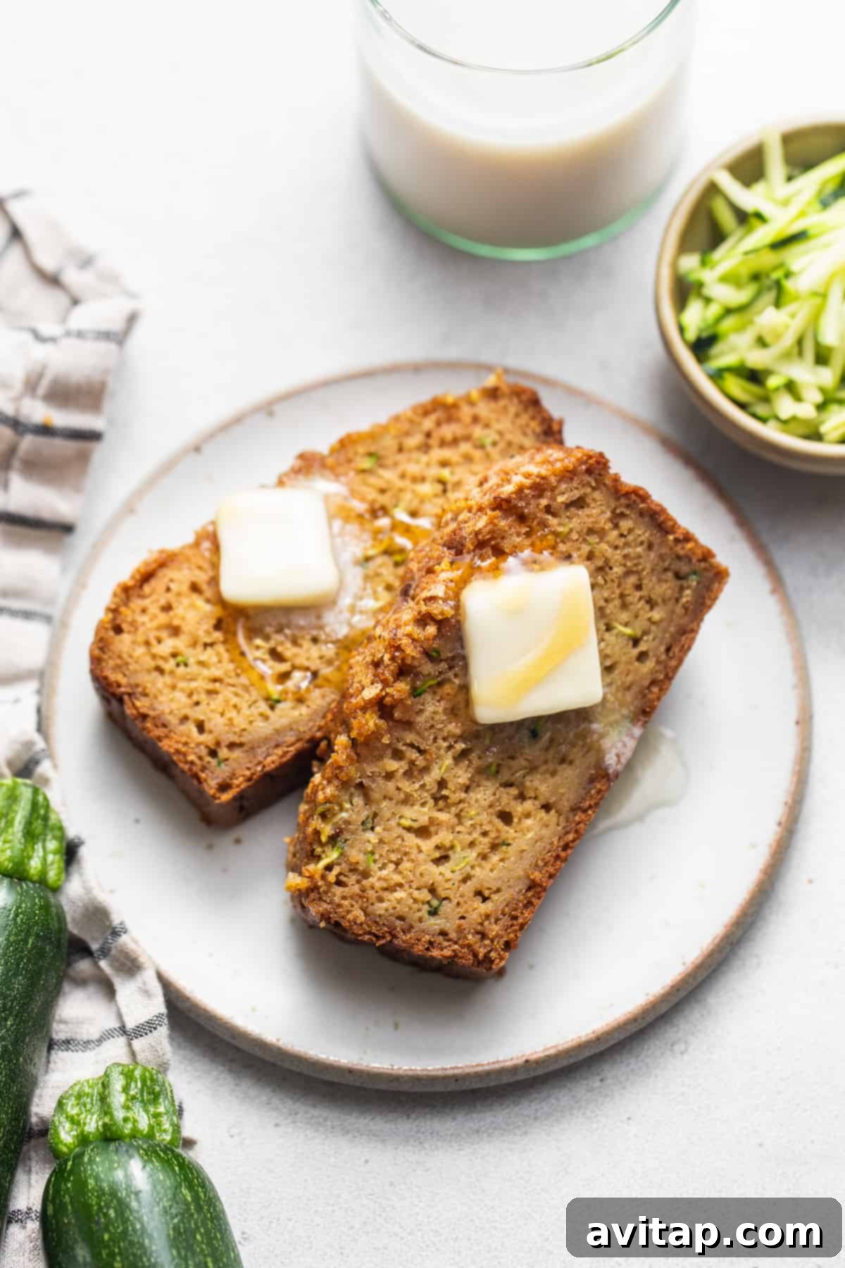 A simple white plate holding two perfectly sliced pieces of zucchini bread, ready to be served or enjoyed with a hot beverage.